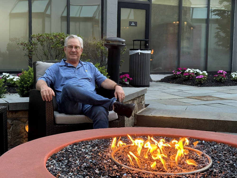Craig Spiesman sitting comfortably near a round fire pit with flames in the foreground