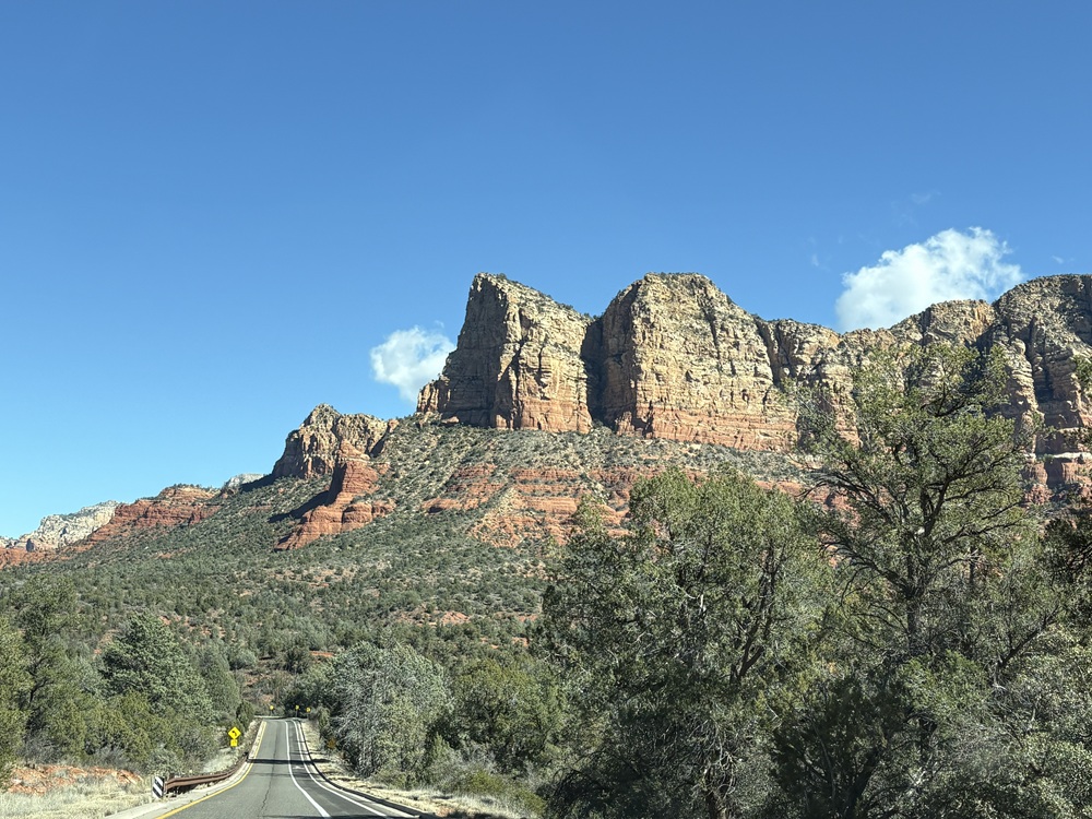 Craig Spiesman photo featuring a winding road below layered red cliffs and green trees