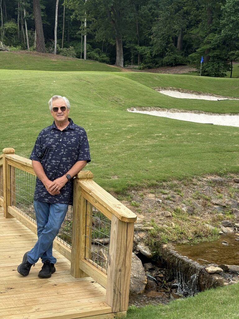Craig Spiesman image featuring a golf green on elevated land with trees and rocky terrain